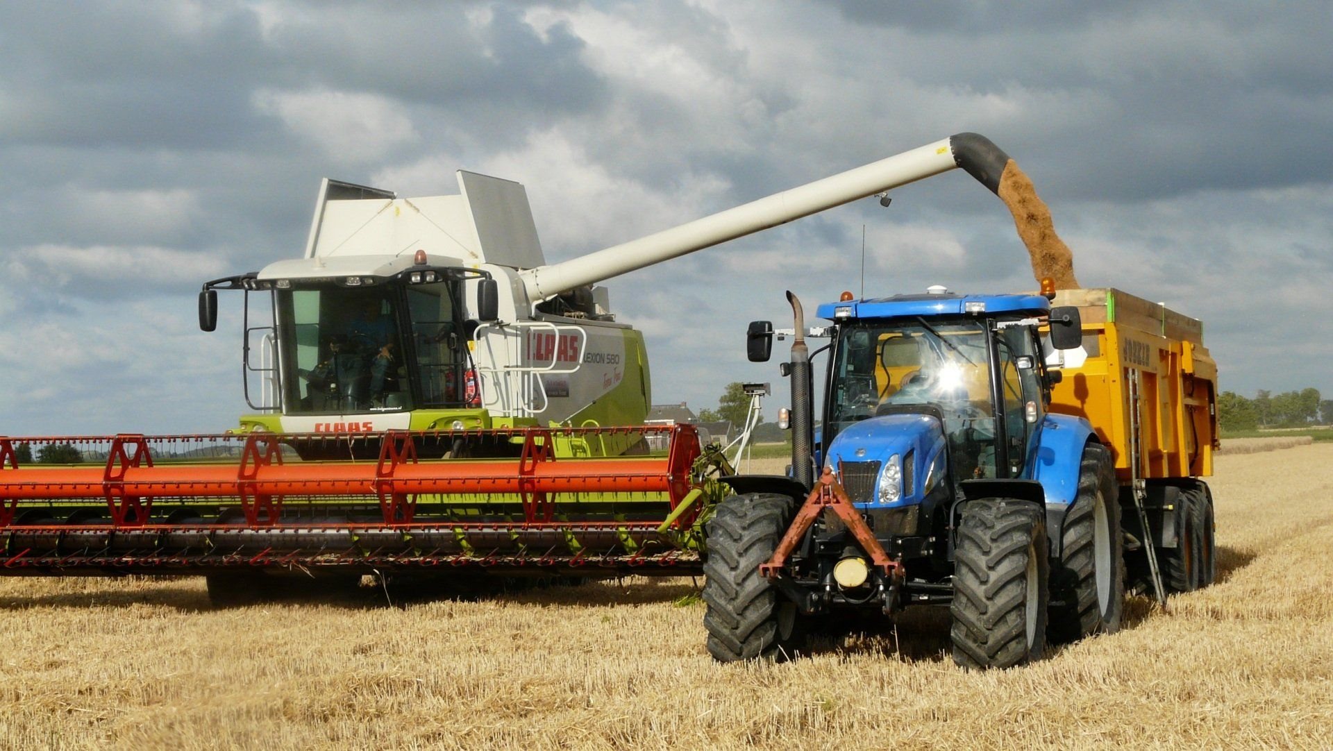 Moissonneuse-batteuse déchargeant le grain dans une remorque tractée par un tracteur bleu